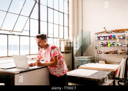 Uomo che utilizza computer portatile durante il lavoro in officina Foto Stock