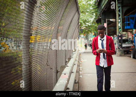 Adolescente indossano uniformi scolastiche usando il telefono mentre camminando sul marciapiede in città Foto Stock