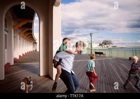 Giocoso famiglia sul lungomare all'esterno dell'edificio contro il cielo nuvoloso Foto Stock