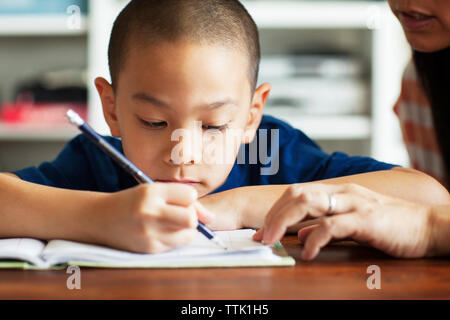 Immagine ritagliata della madre che assiste il figlio a studiare a casa Leggere un libro sul letto di casa Foto Stock