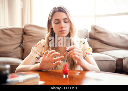 Donna l'applicazione di smalto per unghie seduti contro il divano a casa Foto Stock