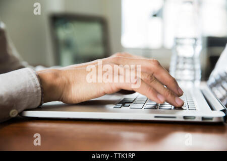 Immagine ritagliata dell uomo d affari con computer portatile a tavola in ufficio creativo Foto Stock