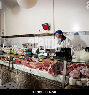 Macelleria sorridente in piedi in vetrina nel negozio di macellaio Foto Stock