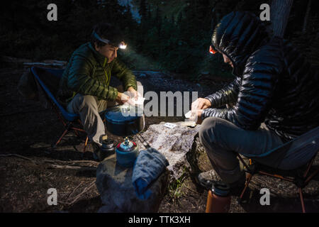 Amici a giocare gioco di carte mentre il campeggio in foresta al tramonto Foto Stock