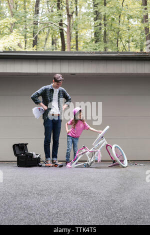 Ragazza mostrando rotture di bicicletta al padre sul marciapiede Foto Stock