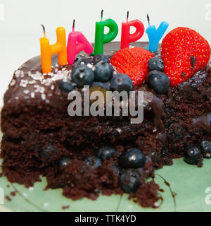 Un parzialmente mangiato torta al cioccolato con soffiato-out candele dicendo felice. La torta è decorata con mirtilli e fragole, glassa di cioccolato e rosa s Foto Stock