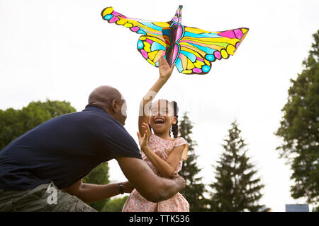 Basso angolo vista di felice padre e figlia giocando con kite contro sky Foto Stock