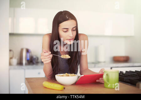 Donna con tavoletta digitale mentre si consuma la prima colazione sul tavolo a casa Foto Stock