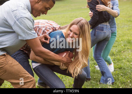 Amici maschi strappi palla calcio da donna sul campo erboso Foto Stock