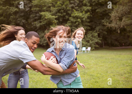 Uomo Donna trazione tenendo palla calcio mentre gli amici in esecuzione in background sul campo Foto Stock