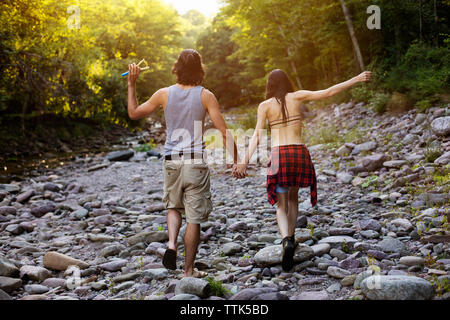 Vista posteriore del giovane tenendo le mani mentre si cammina sulle rocce della foresta Foto Stock