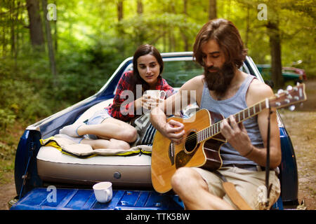 Uomo a suonare la chitarra per ragazza mentre sedendo nel pick-up truck a forest Foto Stock