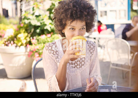 Donna di bere il caffè mentre sedendo nel cafè sul marciapiede Foto Stock