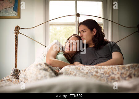 Giovane che guarda lontano mentre vi rilassate sul letto Foto Stock