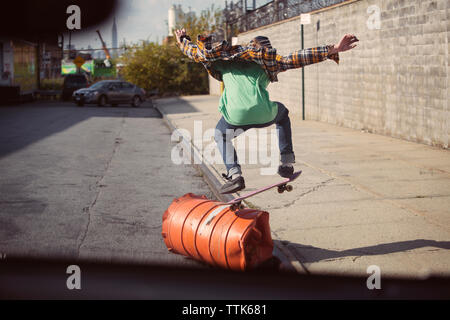 Vista posteriore dell'uomo esecuzione di skateboard stunt oltre la canna su strada Foto Stock