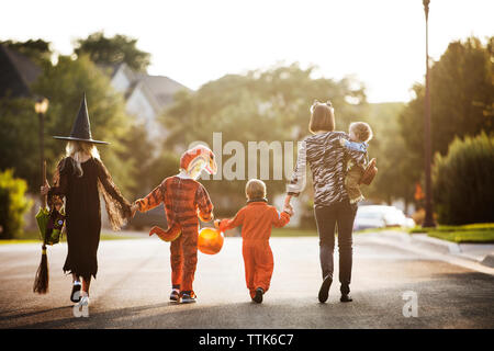 Vista posteriore delle donne con bambini vestiti per la festa di Halloween camminando sulla strada Foto Stock