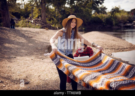 Donna diffusione Coperta picnic sul campo da parte di lago Foto Stock