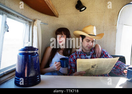 Uomo che legge il giornale mentre la donna che guarda fuori dalla finestra in camper Foto Stock