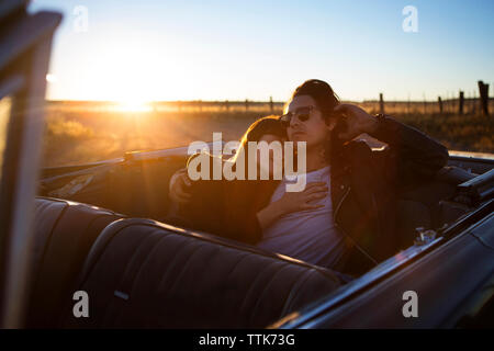 Giovane rilassante sul sedile posteriore nel convertibile durante il tramonto Foto Stock