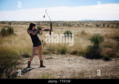 Donna mirando con arco e frecce mentre si sta in piedi sul campo Foto Stock