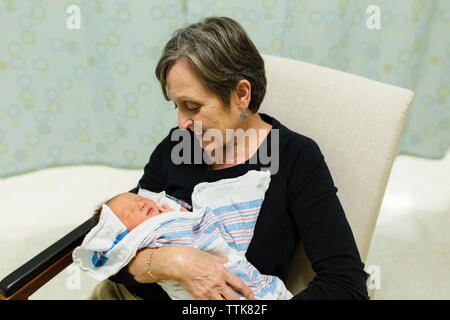 La nonna guarda sorridendo a un nipotino neonato nella stanza di ospedale Foto Stock
