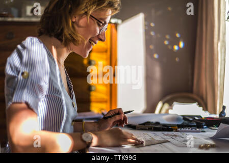 Giovane donna architetto disegno piani e sorridente sulla scrivania Foto Stock