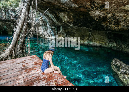 Elevato angolo di visione della donna che indossa un costume da bagno pezzo mentre è seduto sul pontile sul lago Foto Stock