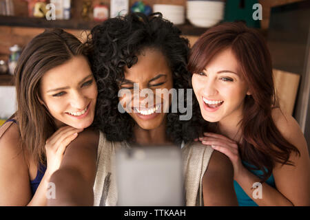Happy amici prendendo selfie permanente, mentre a casa Foto Stock