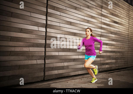 Donna jogging sul marciapiede dalla parete Foto Stock