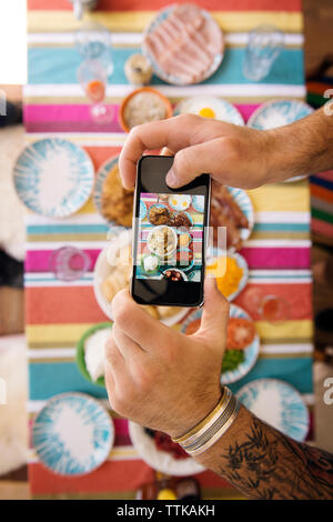 Immagine ritagliata delle mani dell'uomo a fotografare il cibo in tavola Foto Stock