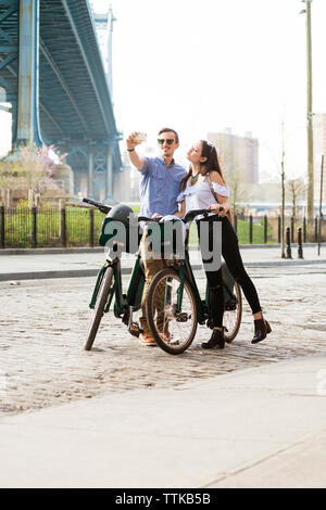 Giovane tenendo selfie stando in piedi con le biciclette su strada Foto Stock