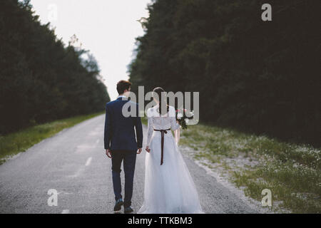 Vista posteriore della sposa e lo sposo camminando sulla strada in mezzo di alberi Foto Stock