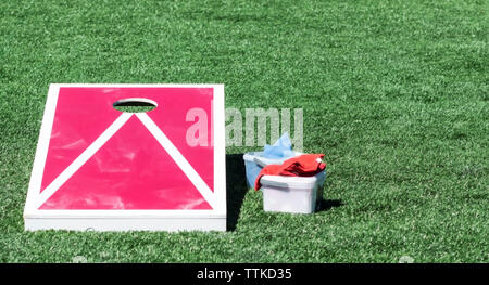 A casa bianca e rossa foro di mais di bordo su un tappeto erboso verde campo con sacchi di fagioli in un contenitore in plastica accanto ad essa. Foto Stock