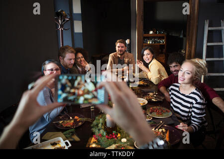 Immagine ritagliata della donna fotografare felici amici mentre godendo pasto Foto Stock