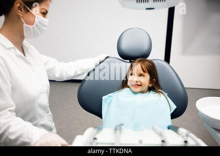 Ragazza sorridente guardando il dentista mentre è seduto in clinica Foto Stock