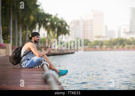 Considerato l'uomo l'ascolto di musica con cuffie e seduta sulla passerella di legno a riverbank Foto Stock