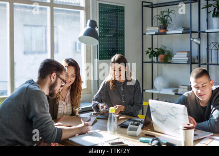 Happy amici che studiano a tavola dalla finestra in aula Foto Stock