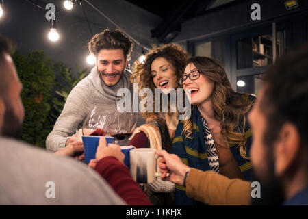 Happy amici tostare un drink nel cortile di notte Foto Stock