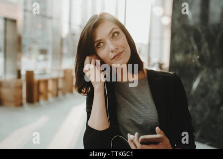 Donna che guarda lontano mentre mettendo a cuffie auricolari presso il cafe Foto Stock