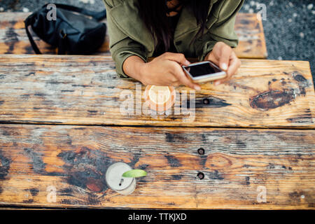 Elevato angolo di visione della donna utilizzando smart phone pur avendo drink al cafè sul marciapiede Foto Stock