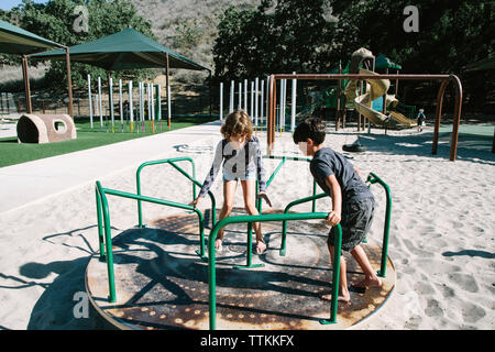 I fratelli a giocare sulla giostra nel parco giochi Foto Stock