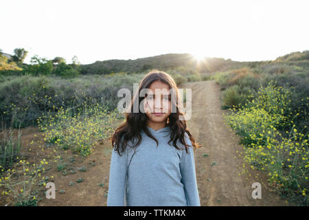 Ritratto di ragazza in piedi sul paesaggio contro il cielo chiaro durante il tramonto Foto Stock