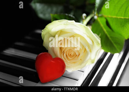 Bella rosa bianca e cuore rosso su tasti di pianoforte, close up Foto Stock