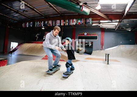 Istruttore di skateboard contiene entrambe le mani di studente scendendo una rampa Foto Stock