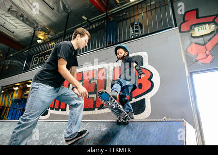 Ragazzo giovane si prepara a scendere in su una rampa di skate con istruttore di guida Foto Stock