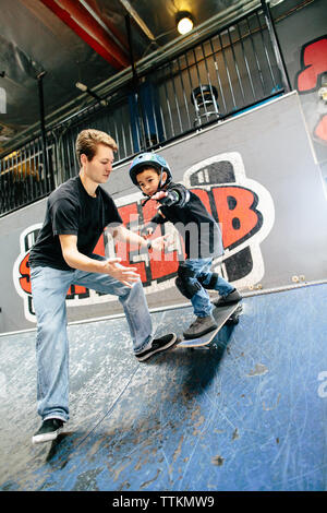 Ragazzo giovane scende in sulla rampa di skate con istruttore pronto per la cattura di lui Foto Stock