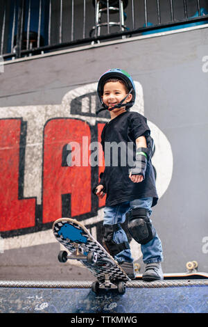 Ragazzo giovane sorride come egli sta per cadere in su una rampa da skateboard Foto Stock