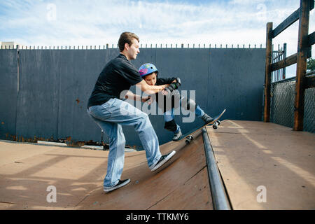 Lo skateboard istruttore aiuta a studente grind su half pipe Foto Stock