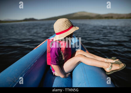 Vista laterale di pensosa ragazza indossando hat mentre è seduto in zattera gonfiabile sul lago Foto Stock