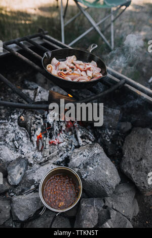 Angolo di alta vista di bacon in una padella essendo cotta sul fuoco aperto al campeggio Foto Stock